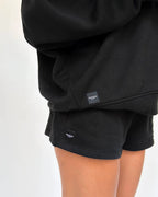 Close-up back view of black sweat shorts showing woven Florence by Mills label at hem