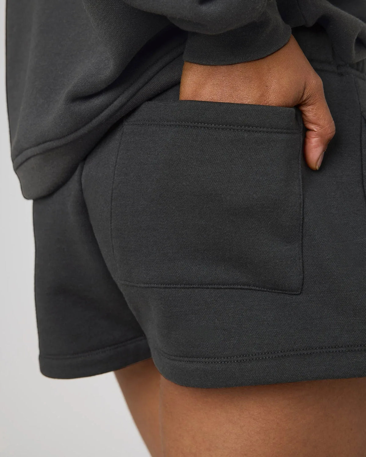Close-up of black sweat shorts back pocket with hand tucked inside, showing stitched patch pocket detail