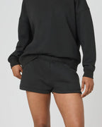 Front close-up of black sweat shorts on model, showing elastic waistband and soft fleece texture