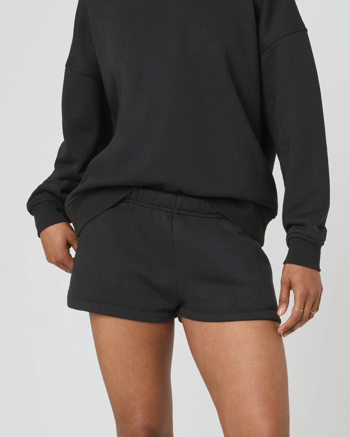 Front close-up of black sweat shorts on model, showing elastic waistband and soft fleece texture