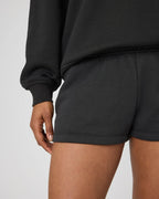 Close-up back view of black sweat shorts hem and waistband next to jumper sleeve
