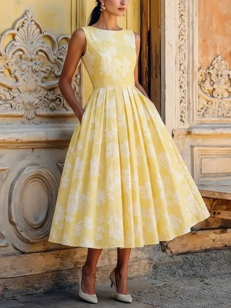 Pale yellow floral midi dress with round neckline and sleeveless bodice, styled with cream heels in front of carved doorway