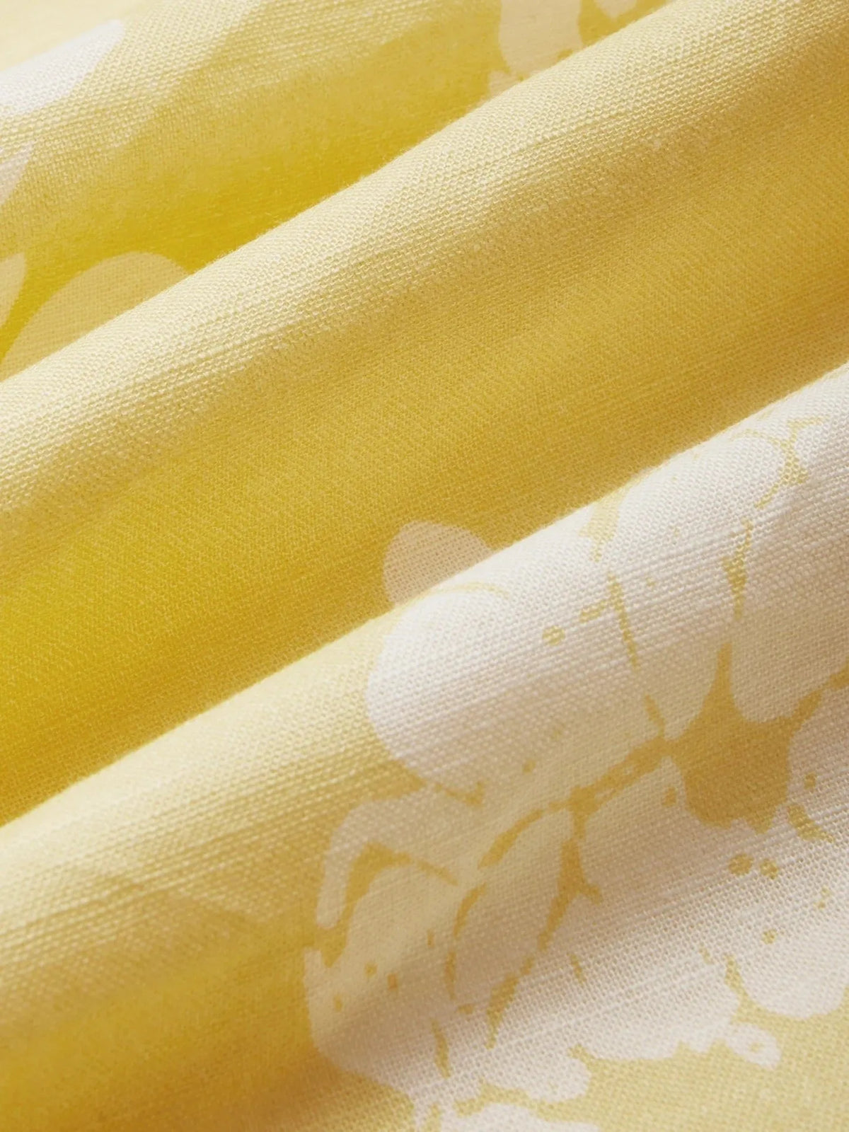 Close-up of lightweight cotton-linen fabric in yellow with white floral print, showing soft folds and woven texture