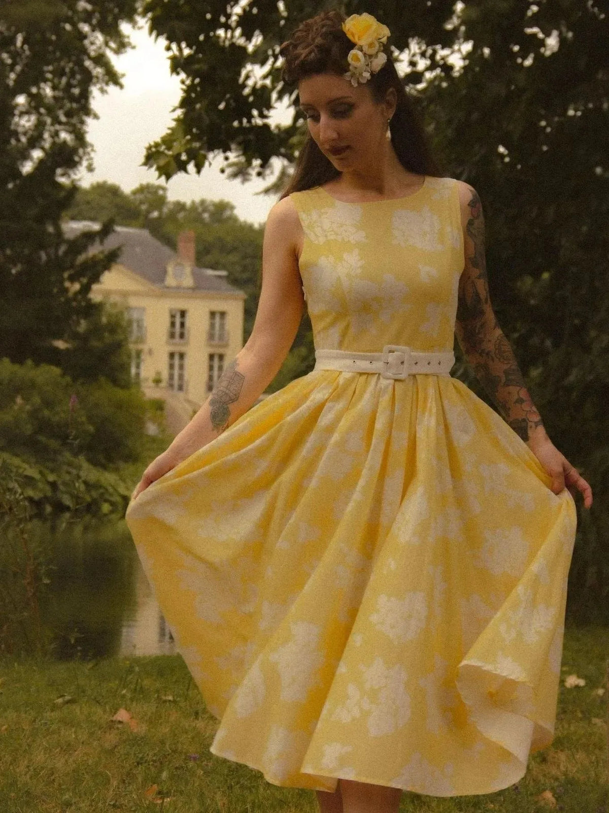 Yellow floral midi dress styled with a white belt cinching the waist, worn with a floral hair accessory in a garden setting