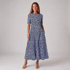 Woman wearing a navy midi dress with a white floral petal print, short sleeves and round neckline, paired with nude heels.