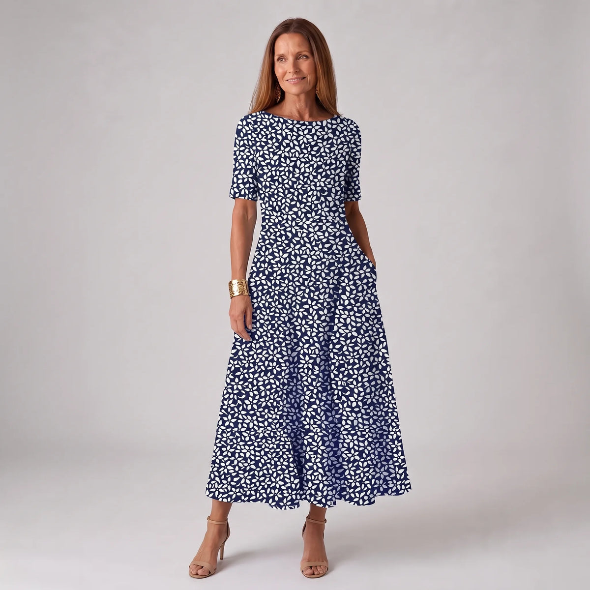 Woman wearing a navy midi dress with a white floral petal print, short sleeves and round neckline, paired with nude heels.