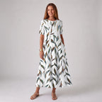 Woman wearing a white midi dress with a watercolour-style green and brown leaf print, short sleeves, styled with gold sandals.