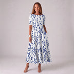 Woman wearing a white A-line midi dress with a navy blue branch and leaf print, short sleeves, paired with nude strappy heels.