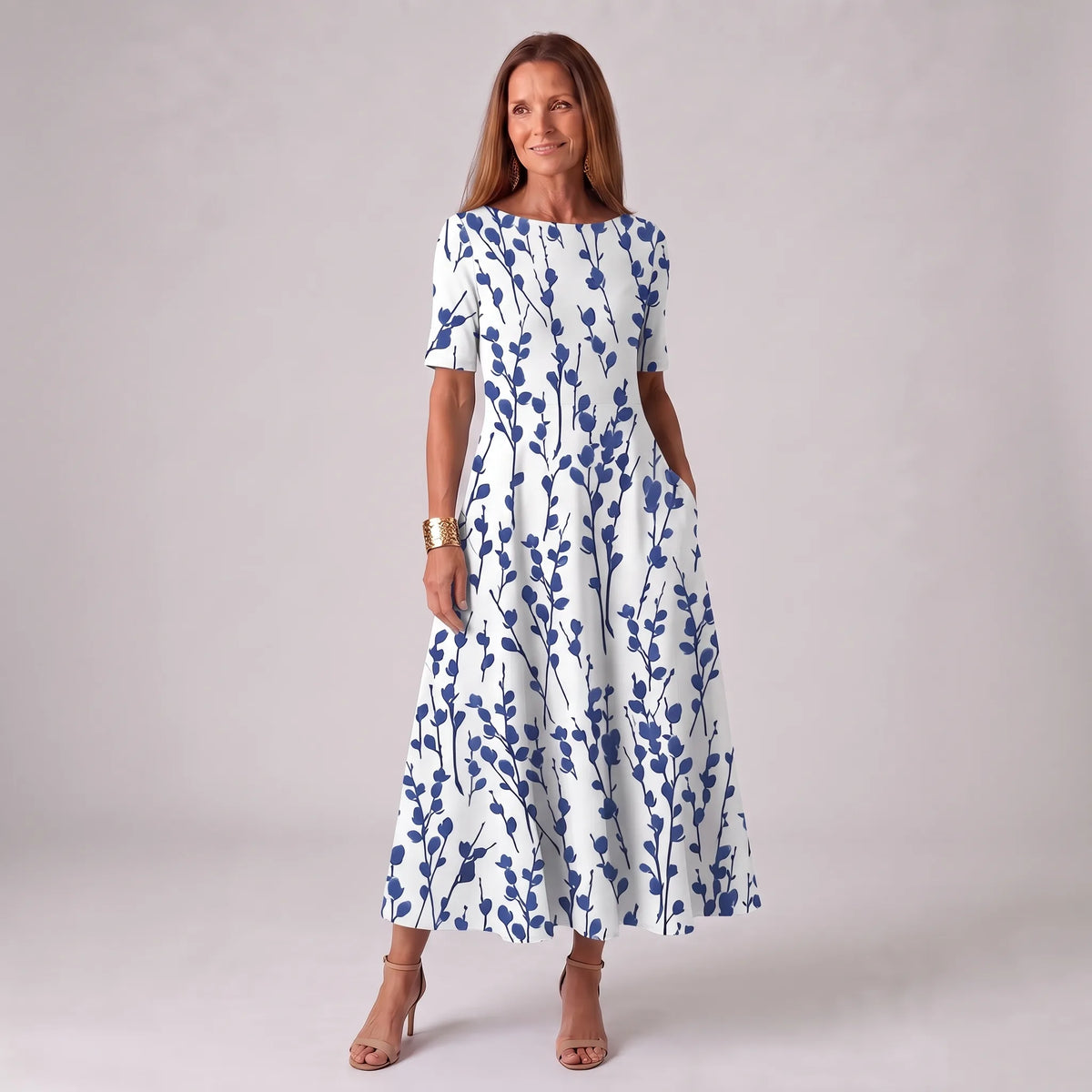 Woman wearing a white A-line midi dress with a navy blue branch and leaf print, short sleeves, paired with nude strappy heels.