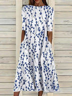 Front view of the white midi dress with navy branch and leaf print, showing the round neckline and side pockets.