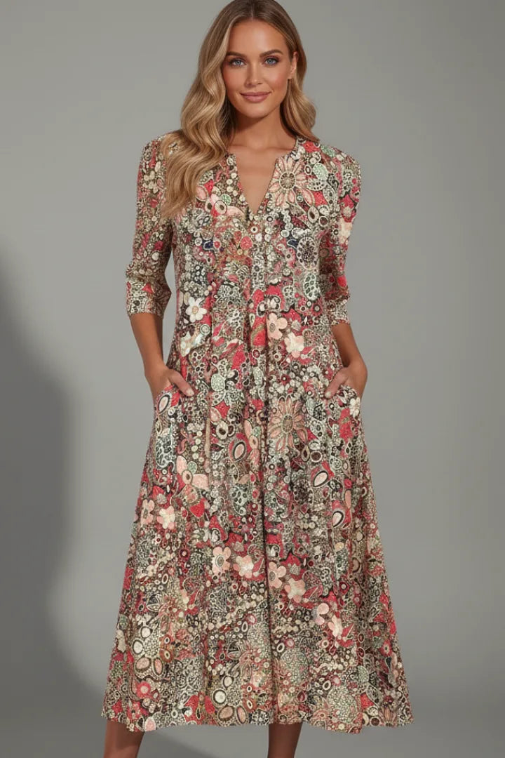 Model wearing the same dress in a red and cream floral print, hands tucked into the pockets