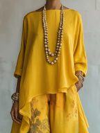 Close-up of the yellow boat-neck tunic top with relaxed three-quarter sleeves and a wooden bead necklace against a textured wall