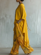 Side profile showing the asymmetric hem of the yellow tunic draping over wide-leg floral pants with a woven bracelet stack
