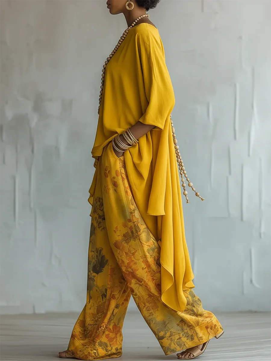 Side profile showing the asymmetric hem of the yellow tunic draping over wide-leg floral pants with a woven bracelet stack