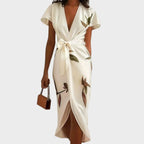 Woman modelling an ivory wrap midi dress with deep V-neckline, tie waist and botanical leaf print, paired with a tan handbag