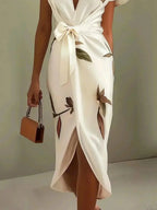 Detail shot of the satin-finish fabric, tie-waist bow and flutter sleeve on the ivory wrap dress