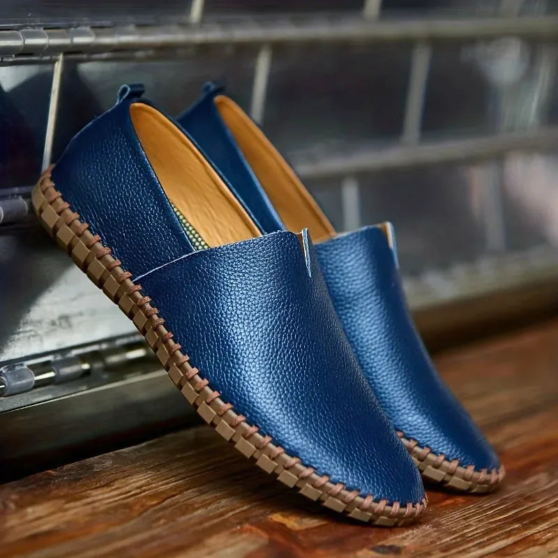 Pair of royal blue pebbled leather loafers with contrast stitched sole, angled view on a workshop ledge