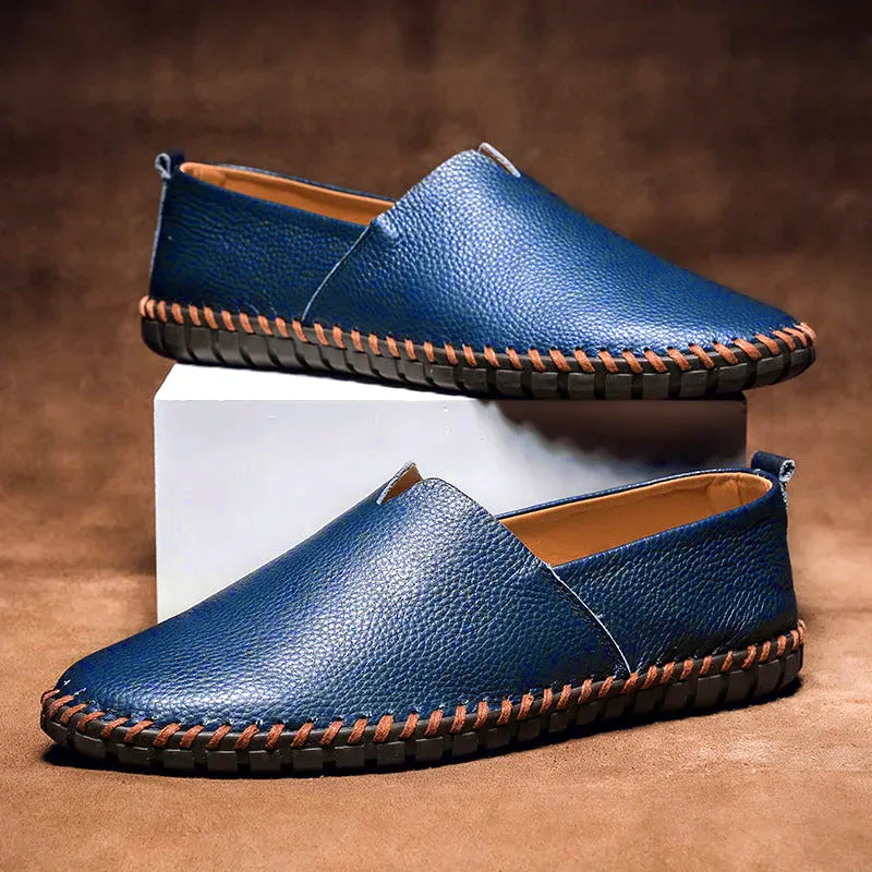 Side profile of royal blue leather loafers stacked on a white block against a brown backdrop