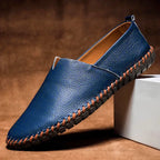 Single royal blue leather loafer shown from the side, resting against a white block