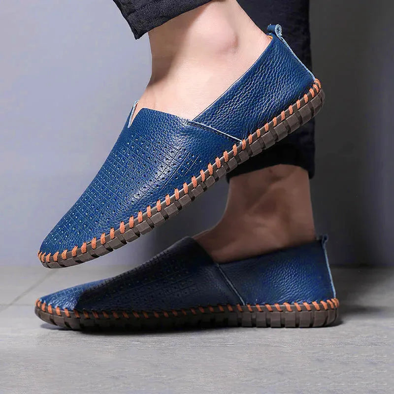 Man wearing royal blue leather loafers barefoot, standing on a tiled floor with perforated toe detail visible