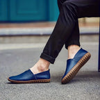 Man wearing royal blue leather loafers with rolled black trousers while seated outdoors