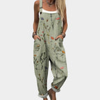 Woman wearing a sage green botanical print jumpsuit with wide straps, cuffed hems and sandals, hands in front pockets