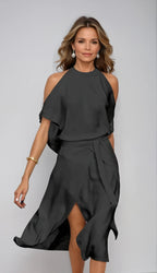 Front view of a woman wearing a black halter neck wrap midi dress with cold shoulder sleeves and an asymmetrical hem