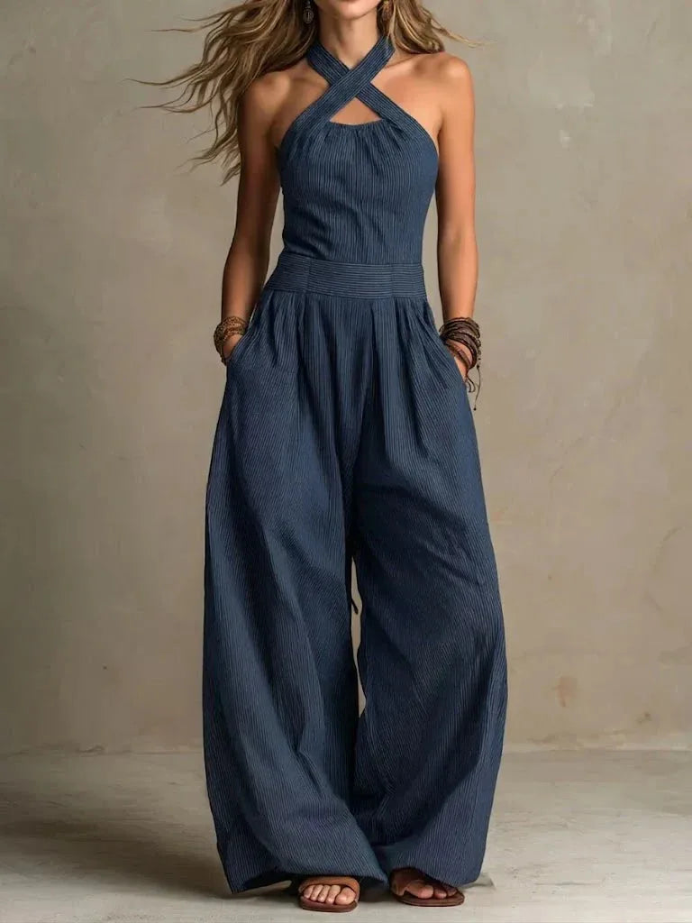 Navy pinstripe halter jumpsuit featuring a crossed front neckline, side pockets and flowing wide legs