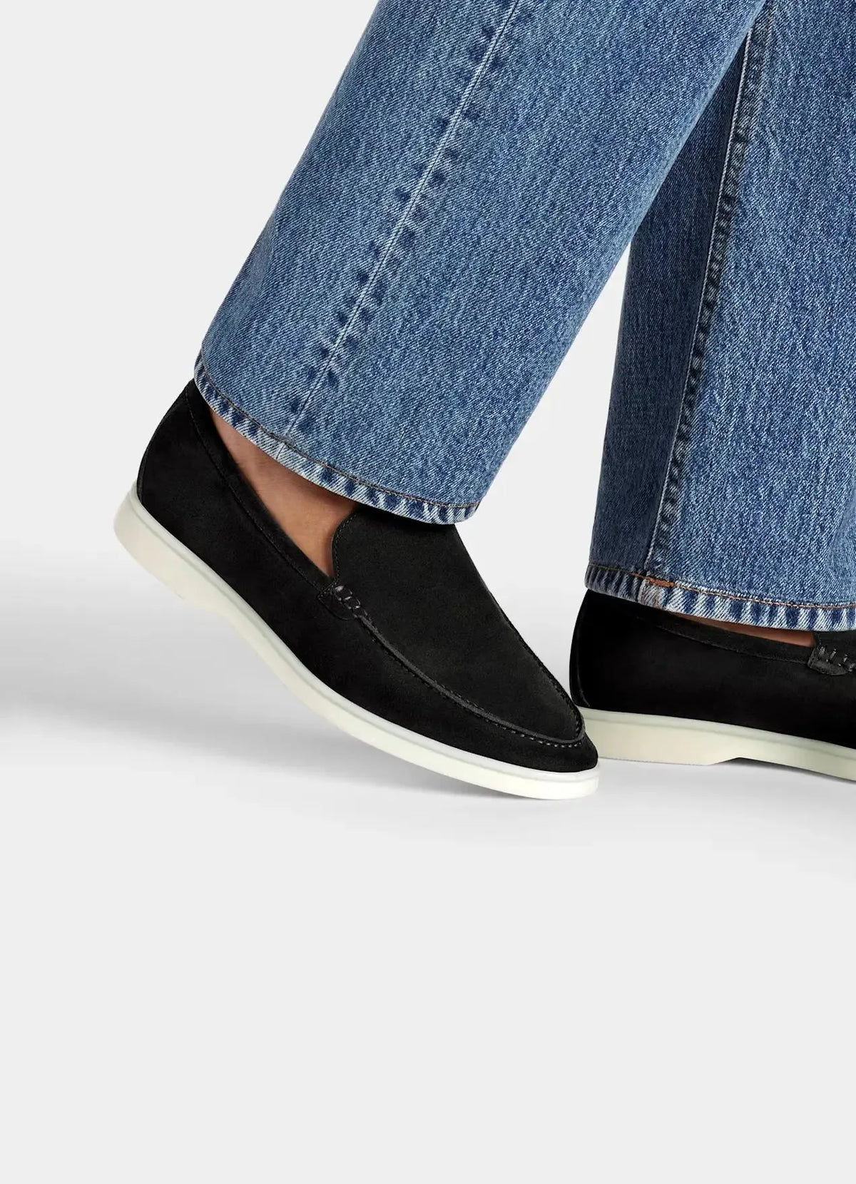 Close-up of a model's ankle wearing black suede loafers with wide-leg denim jeans