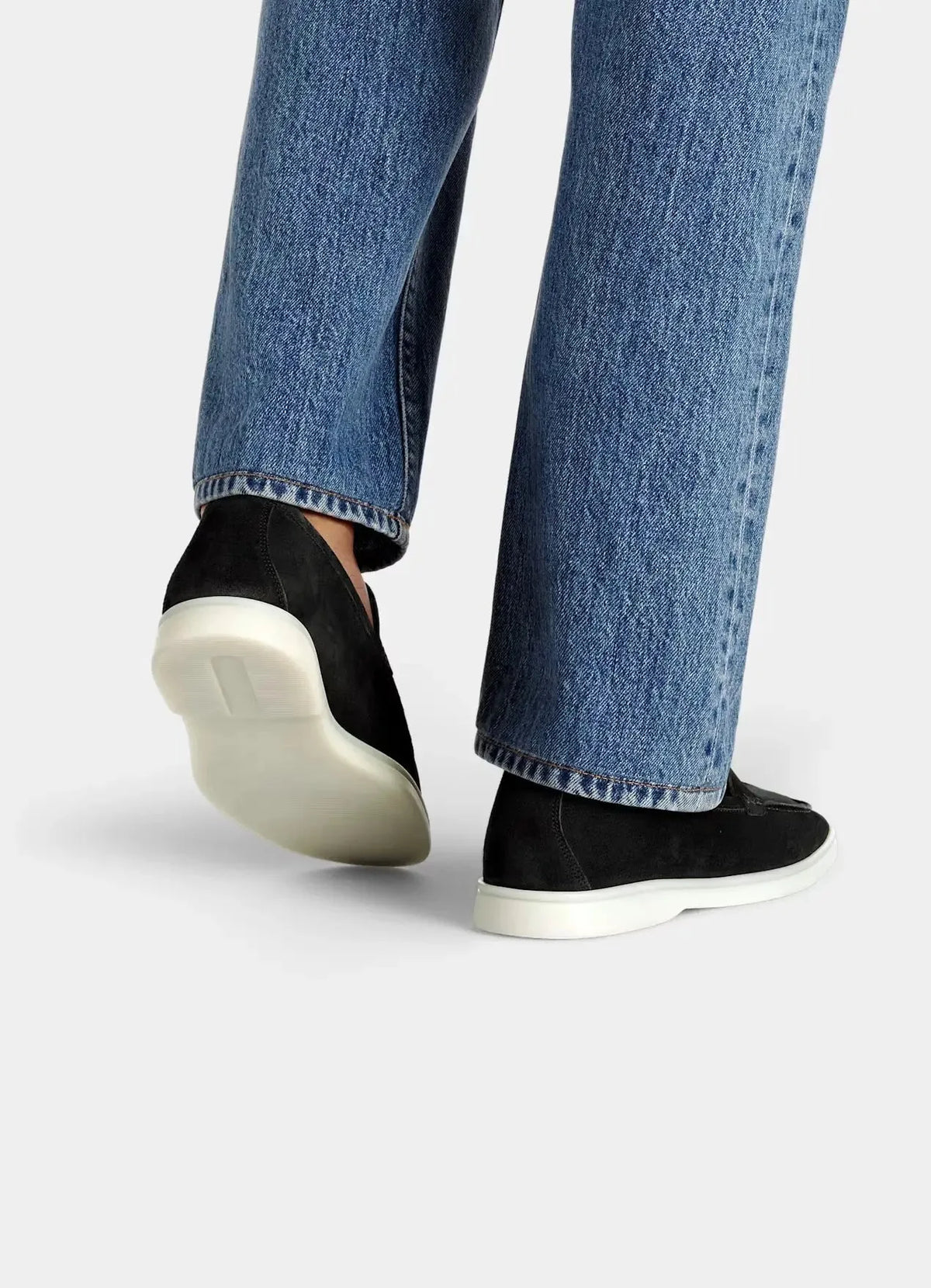 Rear view of black suede loafers worn with denim, showing the heel shape and white outsole