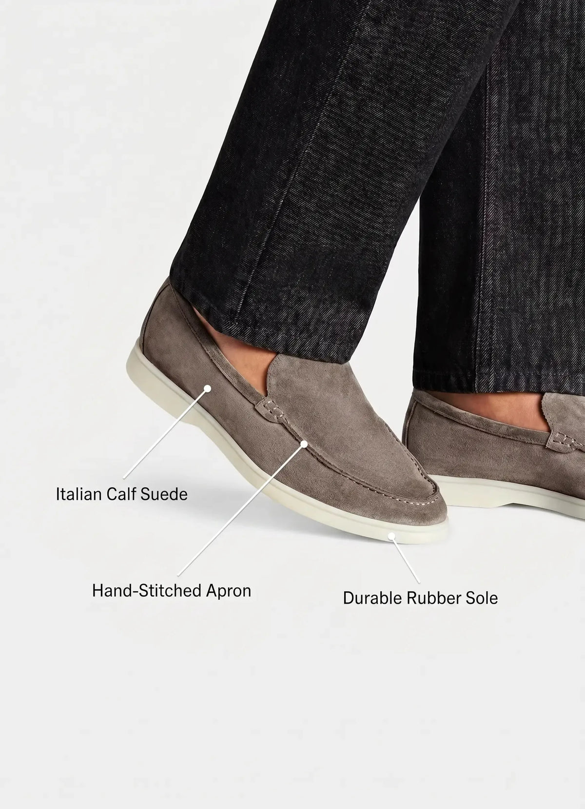 Detail shot of grey suede loafers on foot with labels pointing to calf suede, stitched apron, and rubber sole