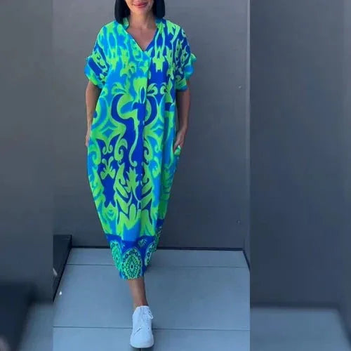 Woman wearing a green and blue abstract print kaftan midi dress with short sleeves and V-neck, styled with white sneakers