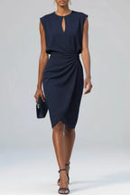 Front view of a navy blue midi dress with cap sleeves, keyhole cutout and draped ruched waist, styled with a navy clutch bag