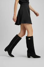 Model walking in black foldover knee-high boots paired with a black mini skirt, showing boots in motion