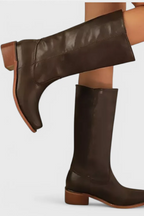 Close-up side profile of dark brown knee-high leather boots on a model, showing stacked heel and pointed toe shape