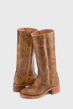 Front view of weathered tan leather knee-high boots with visible natural grain and stacked heel