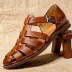 Light brown leather fisherman sandal with visible grain texture and tan insole, propped against a small wooden stool.