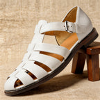 White leather fisherman sandal with woven strap detail and silver buckle, shown balanced on a wooden stool.