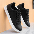 Pair of black leather sneakers resting against a wooden wall, showing low-top silhouette and white soles