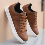 Close-up side view of brown leather sneakers leaning against a wall, showing lace detail and heel panel