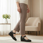 Side view of a woman walking in black leather Mary Jane wedge shoes paired with tailored trousers
