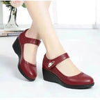 Close-up of burgundy leather Mary Jane wedge shoes showing the stitched trim and rhinestone buckle detail