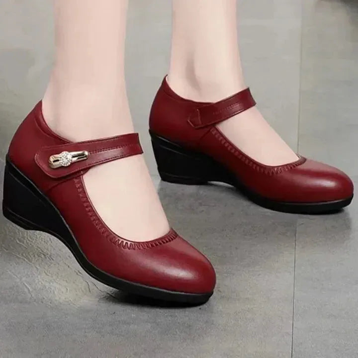 Angled view of burgundy leather Mary Jane wedge shoes with contrast black wedge sole on a tiled floor