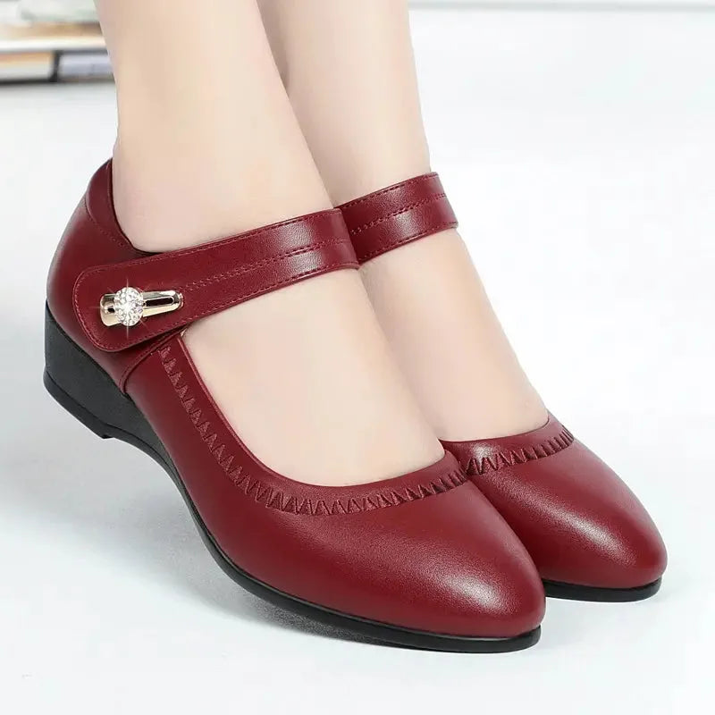 Close-up of black leather Mary Jane wedge shoes showing the hook and loop strap with crystal buckle