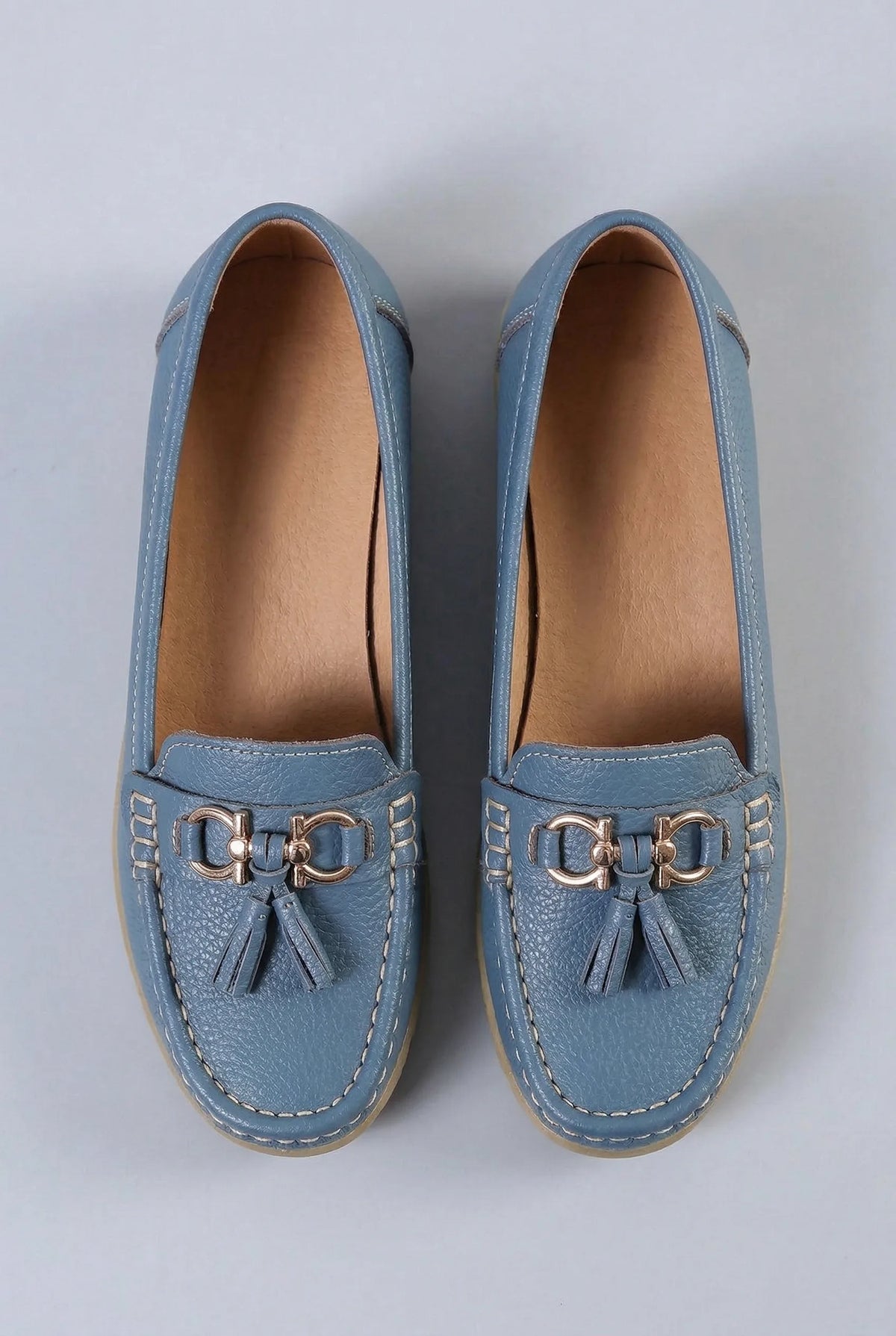 Top-down view of a pair of dusty blue leather loafers showing the tassel hardware and contrast stitching