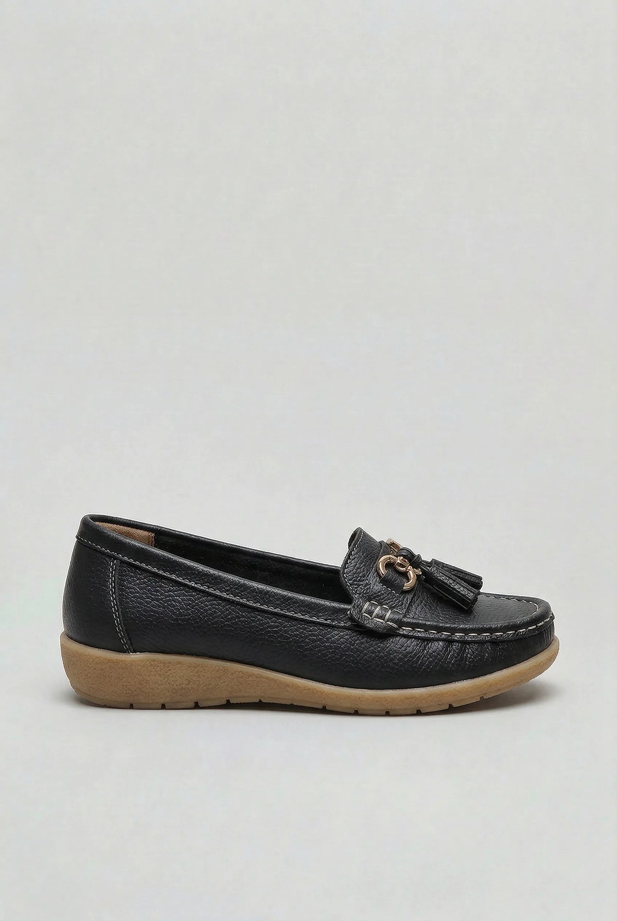 Side profile of a black leather loafer with tassel detailing and a textured rubber wedge outsole