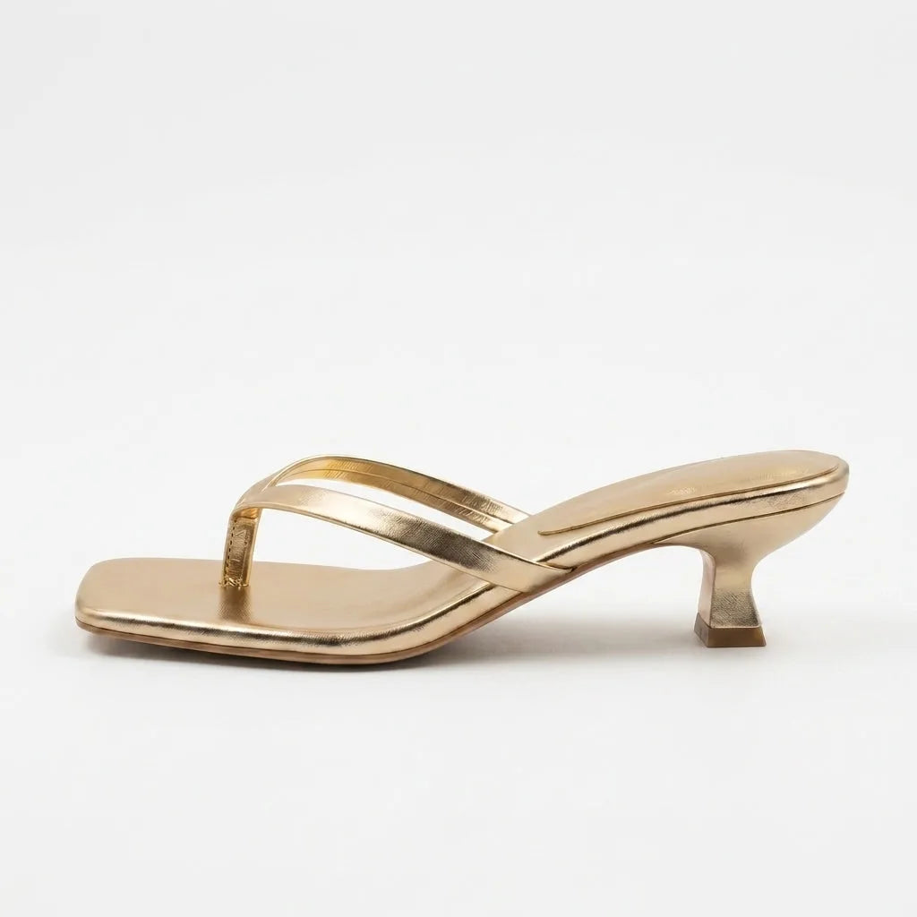 Side view of a metallic gold thong sandal featuring a low kitten heel and padded square toe bed