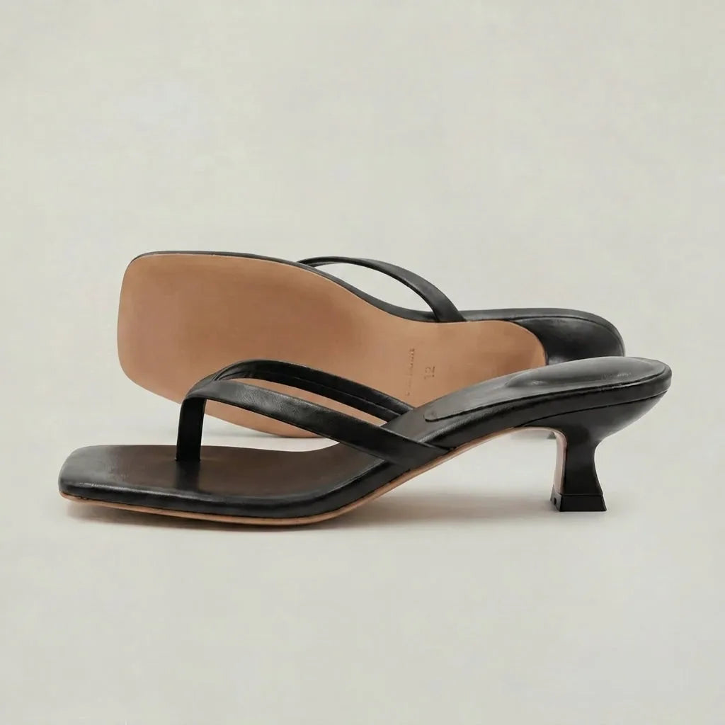 Close-up of a model's feet walking in black leather thong sandals with a low kitten heel