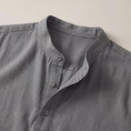 Close-up of the band collar and button placket on the grey shirt, highlighting the woven linen texture and stitching.
