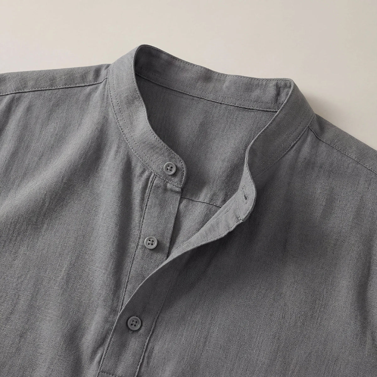 Close-up of the band collar and button placket on the grey shirt, highlighting the woven linen texture and stitching.